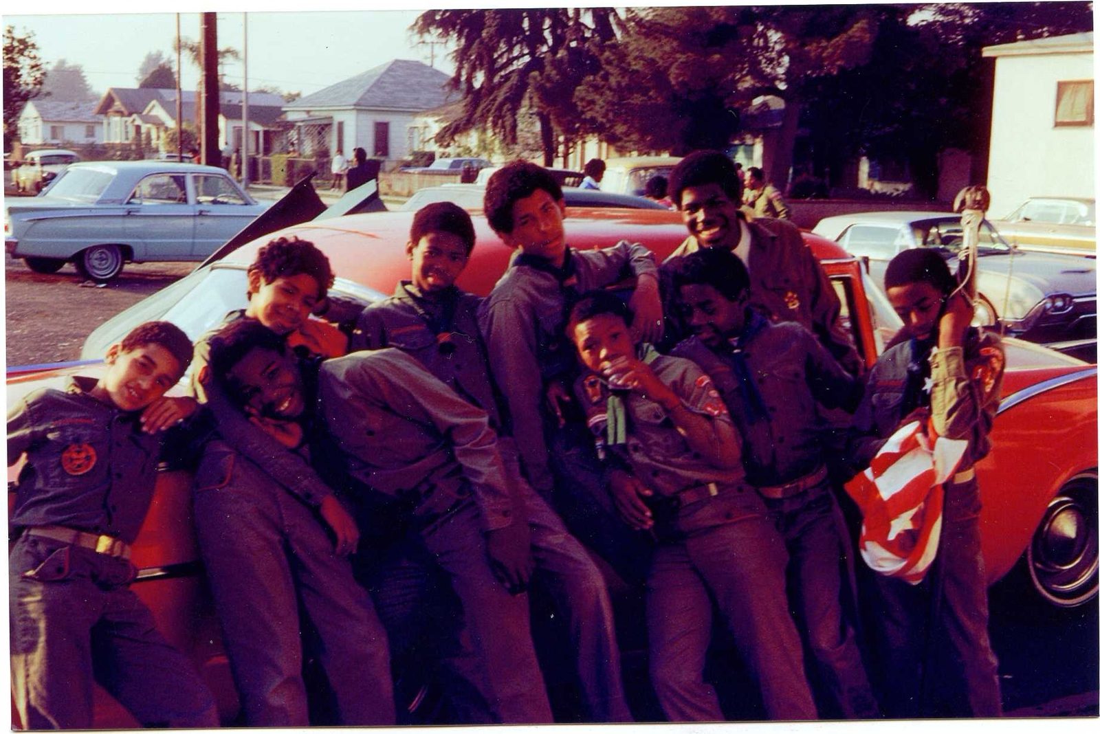Scouts in uniform crowded together against a car on a residential street