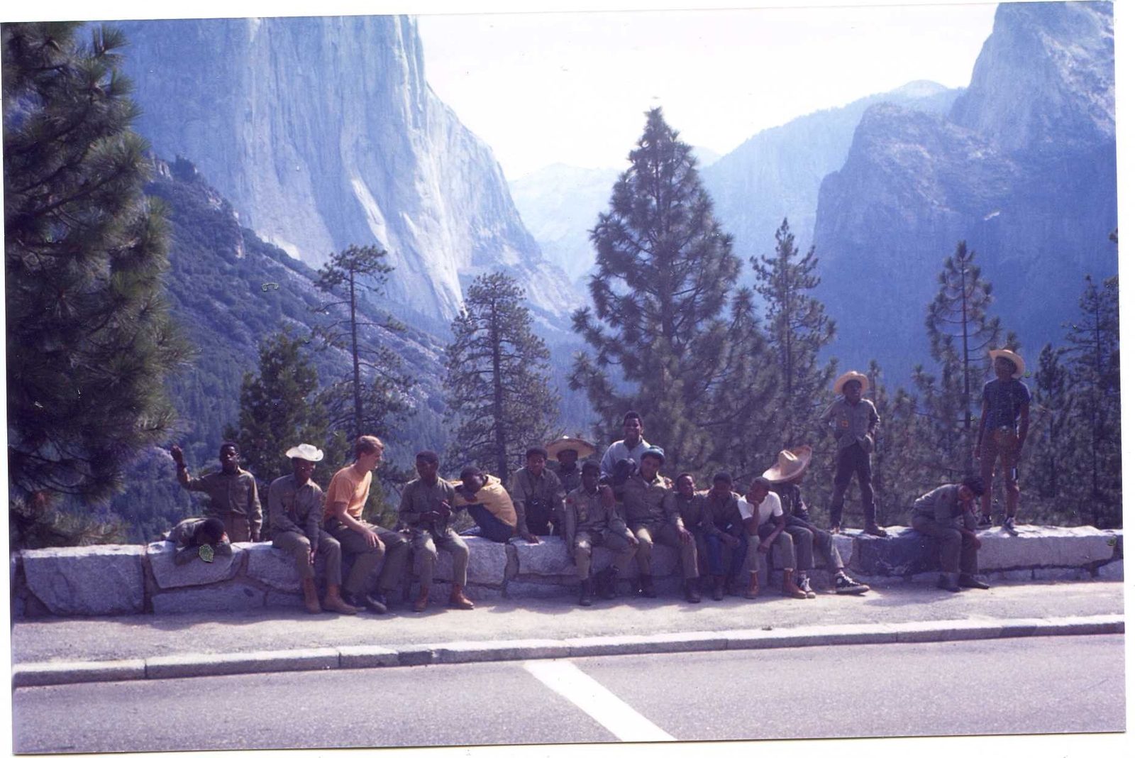 Scouts sitting along a stone wall by the road, the granite cliffs of Yosemite Valley behind them